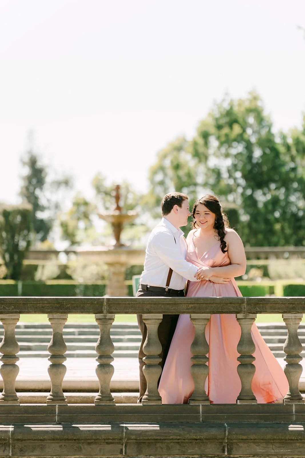 Saira and Matthew leaning together at a stone balustrade above the garden fountain.