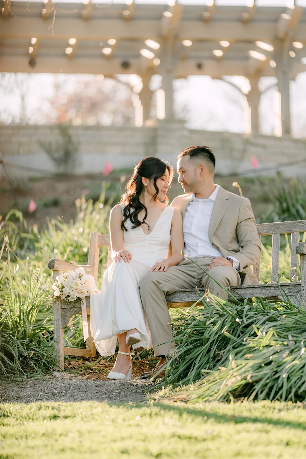 Kim and Vincent seated on a garden bench beneath a wooden pergola.