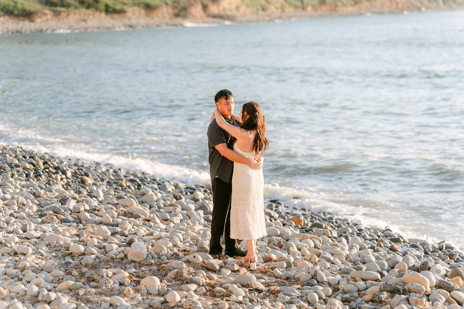 Victoria and Andrew embrace at the water's edge.