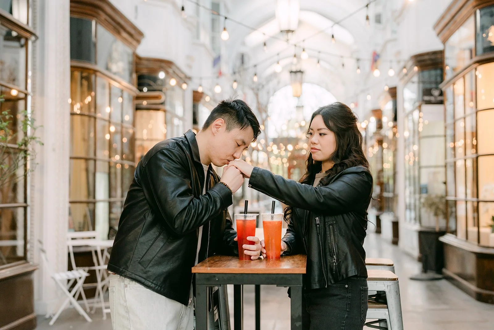Emily and James share their drinks at a café table under the arcade's glass ceiling.