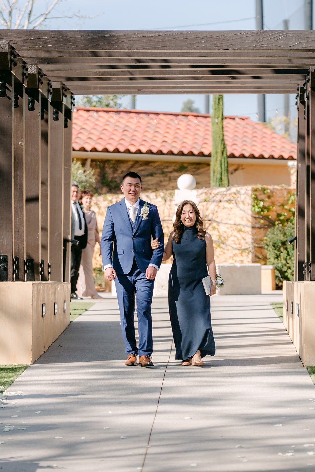 Alex walking down the aisle with a family member under the pergola