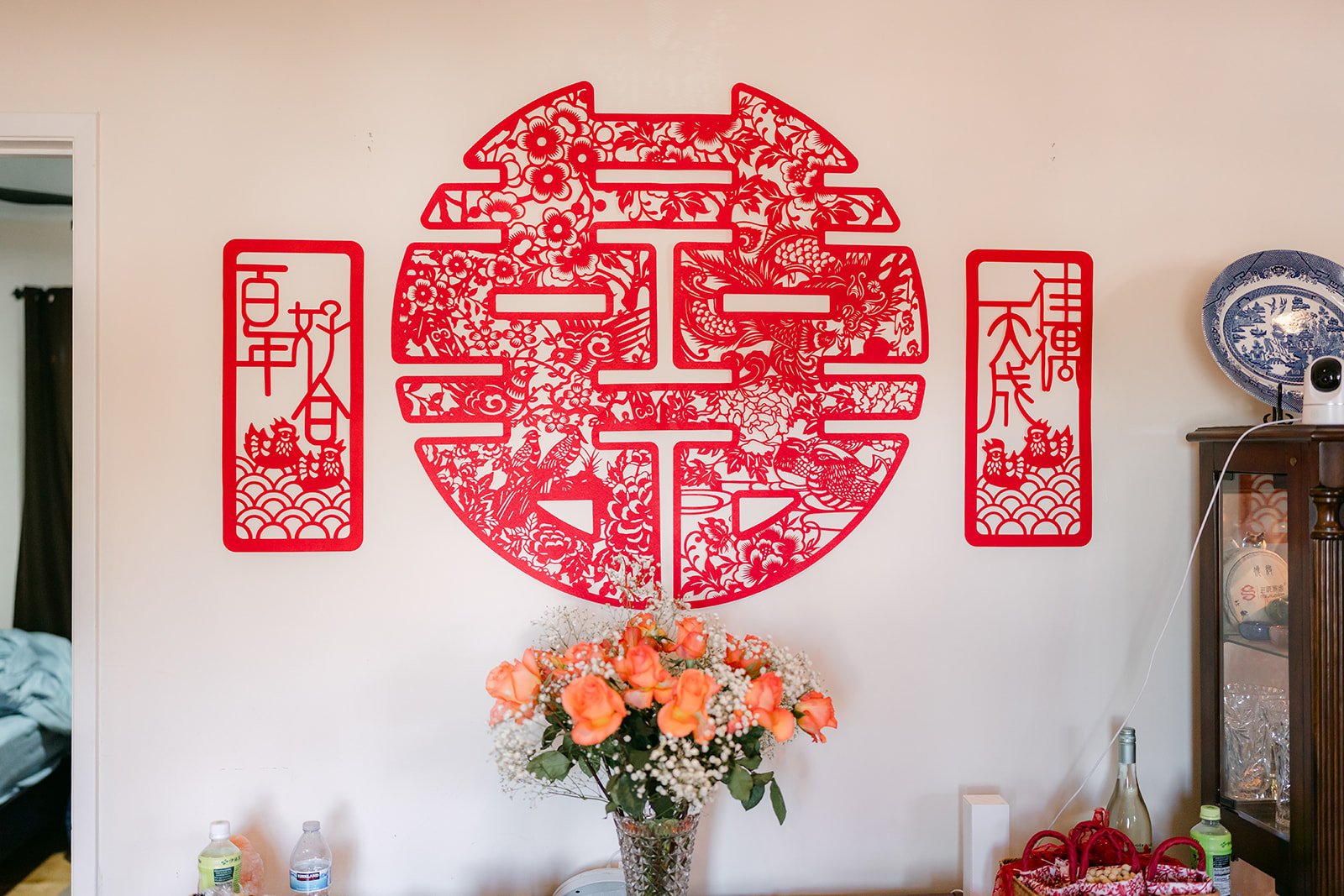 A large red double happiness papercut with couplets above a family's living room cabinet.