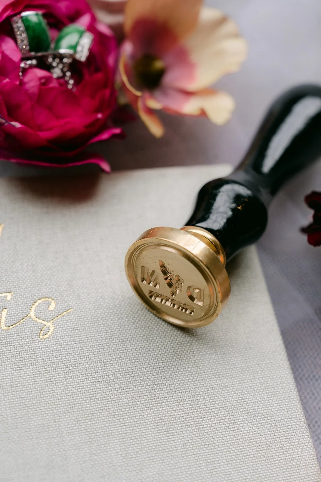 Close-up of the gold wax seal stamp beside a burgundy rose.