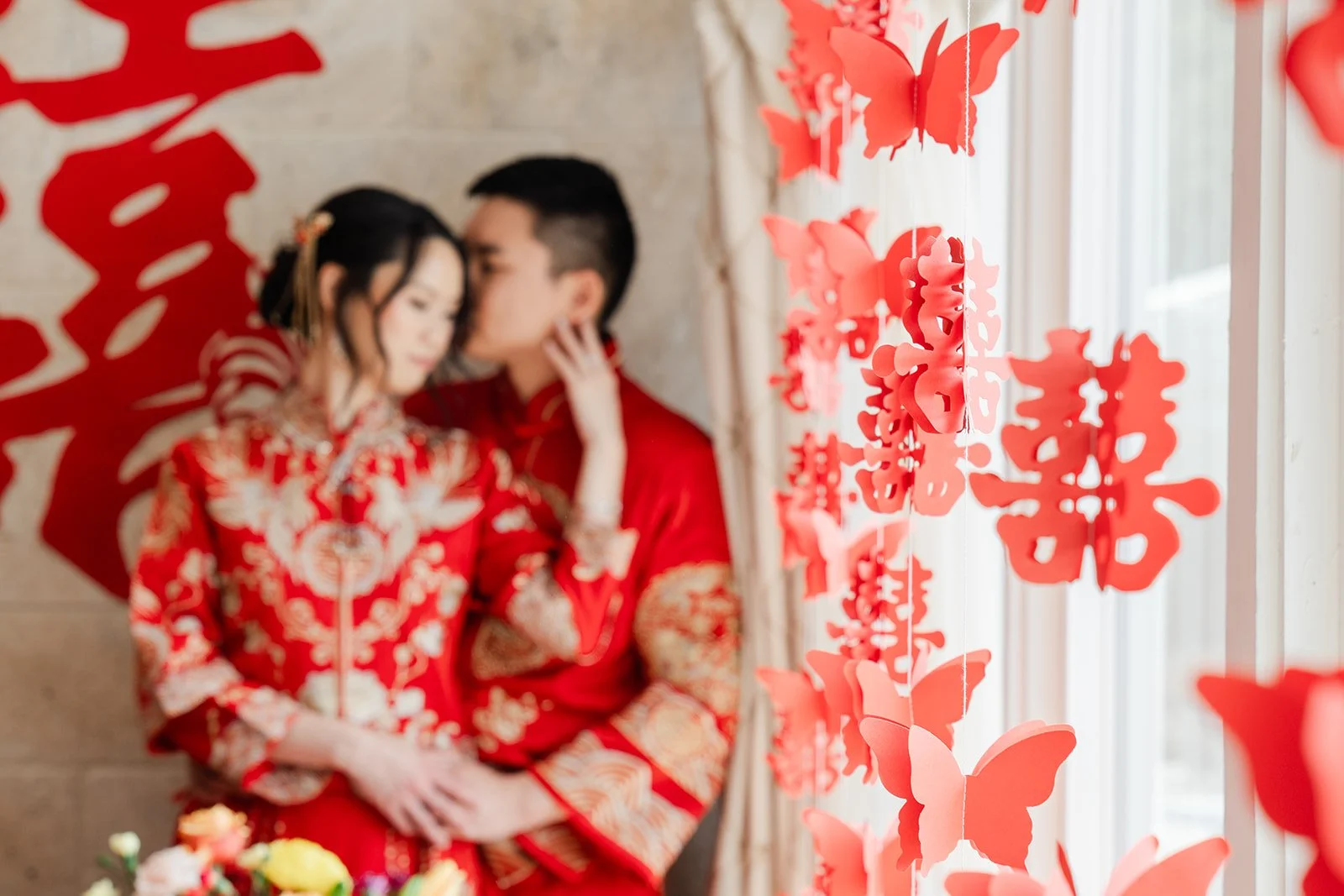 Henrik kissing Bridgette's forehead under double happiness papercuts and red butterflies.