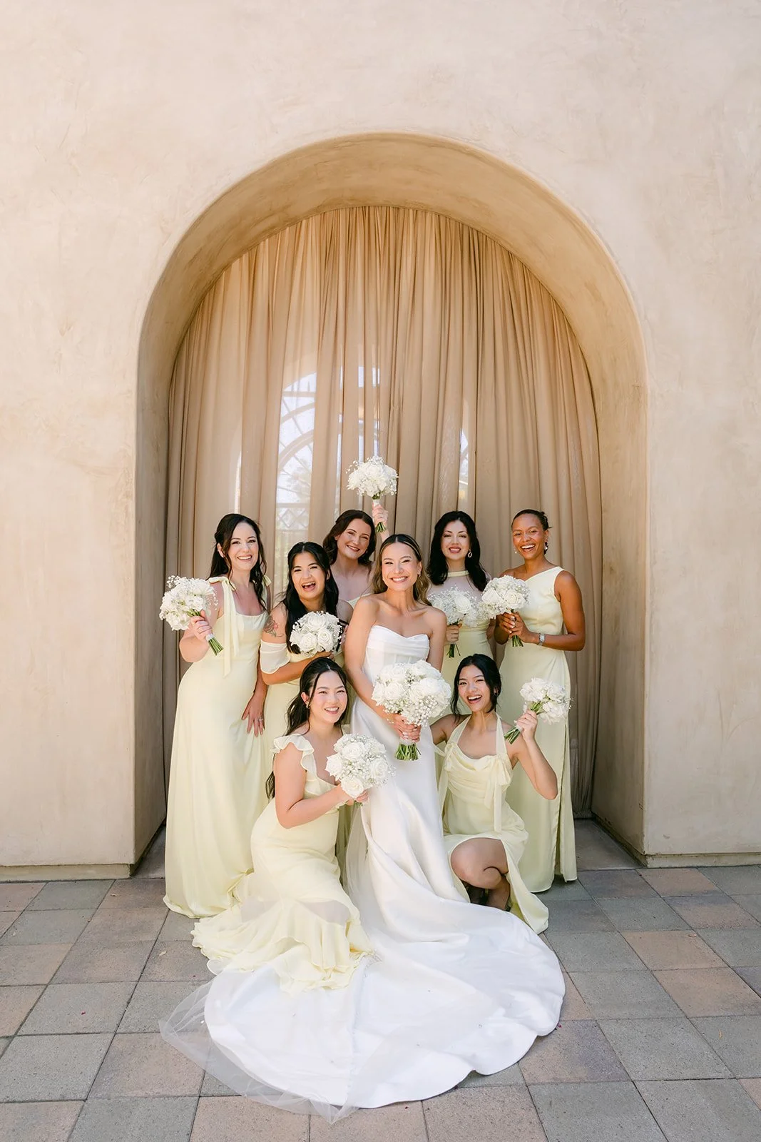 Bride sitting with her bridesmaids in front of a curtained arch at Serra Plaza