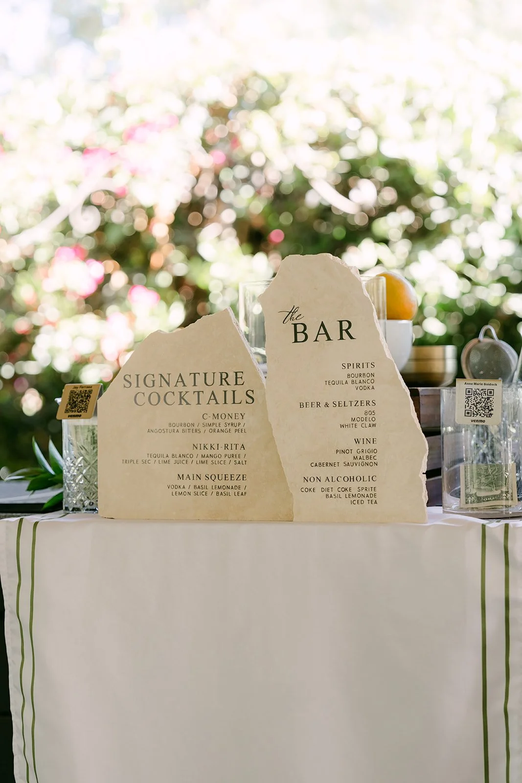 Signature cocktail menu on the bar beside blush and ivory florals.