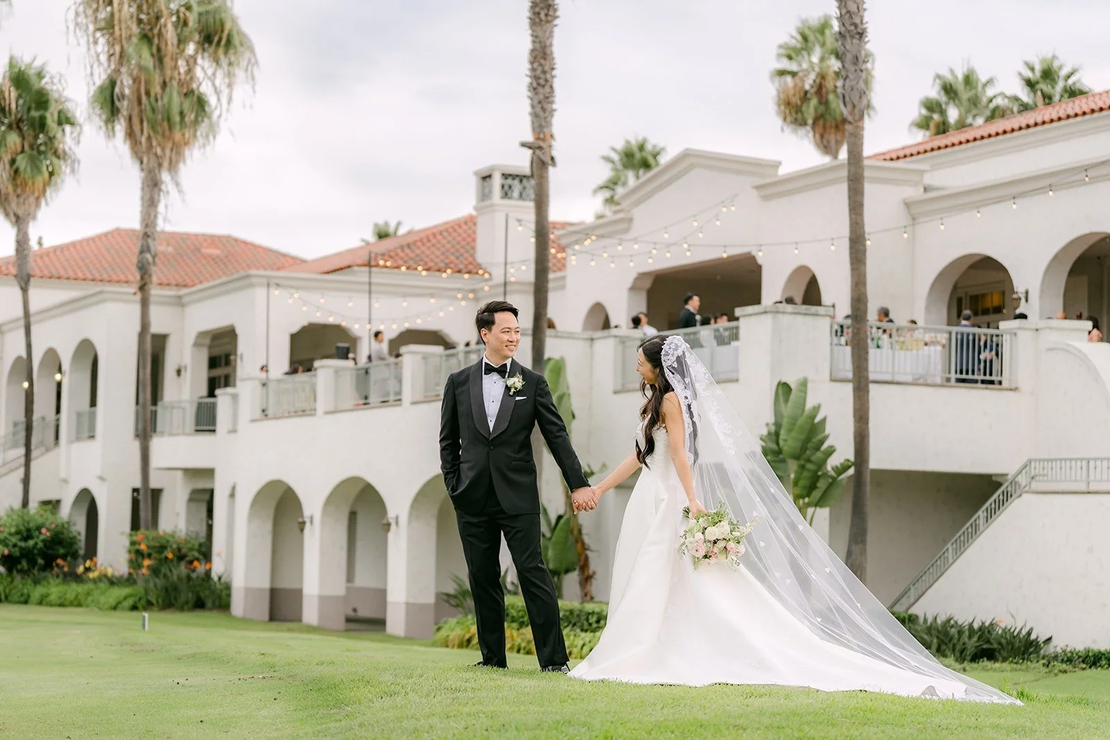 Kristine and William on the lawn in front of the white Los Coyotes clubhouse and palm trees