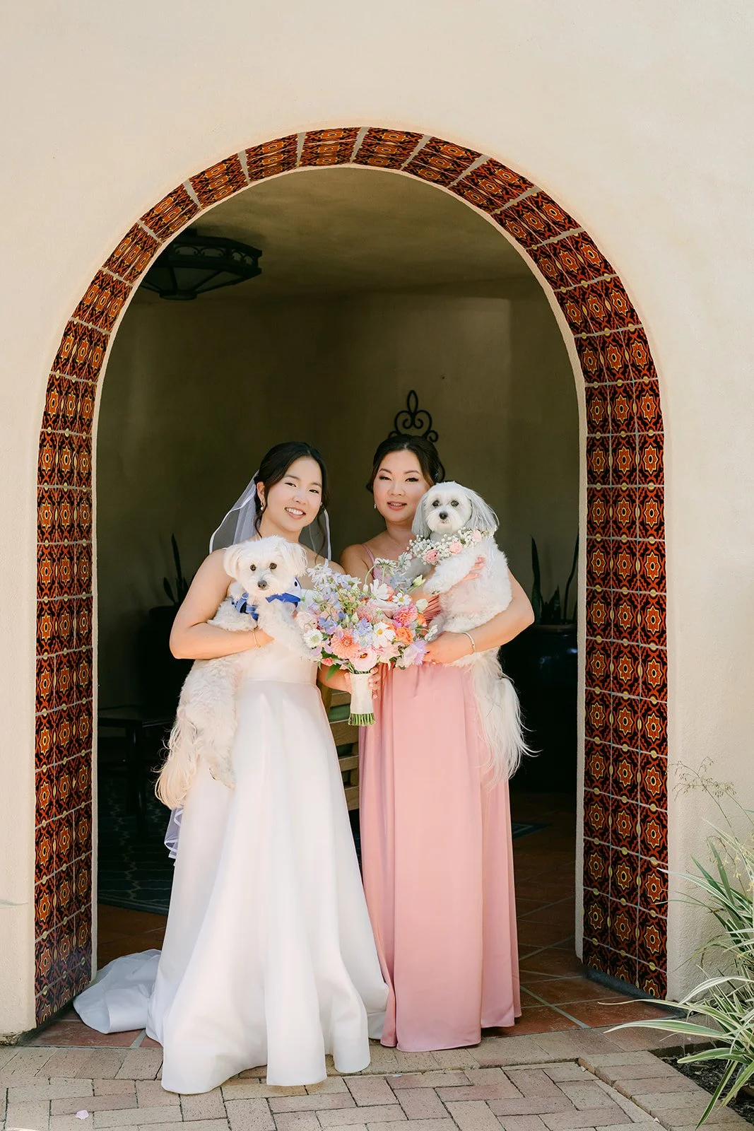 Saya and a bridesmaid holding their pups under the tiled archway