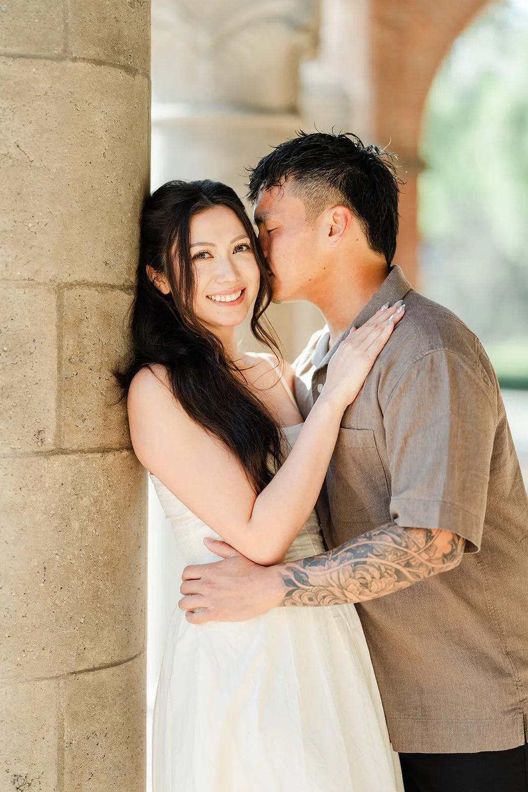 Andrew leans in to kiss Victoria against a stone column.