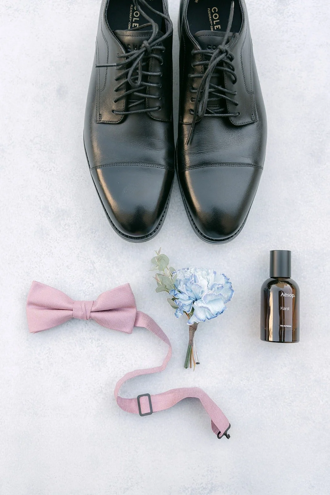 Brandon's black dress shoes, pink bow tie, suspenders and boutonniere in a flat lay at The Headquarters