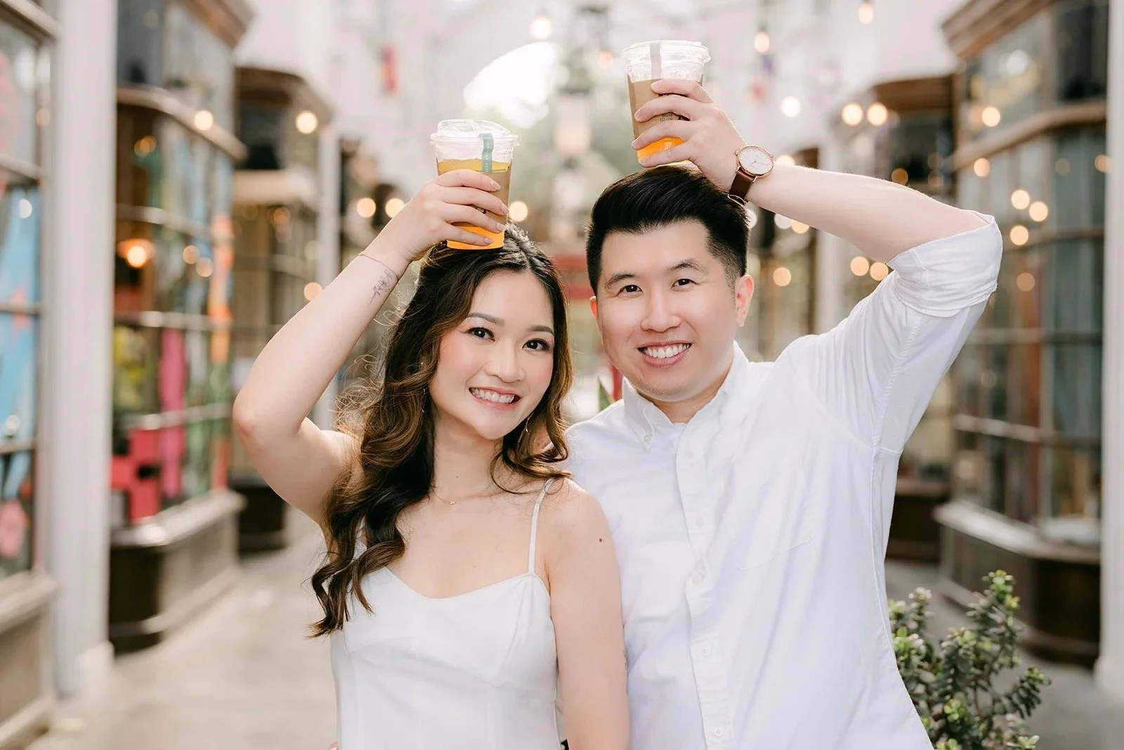 Amanda and San raise their drinks beneath the glass ceiling of the Burlington Arcade in Pasadena, photographed by One and Only Production.