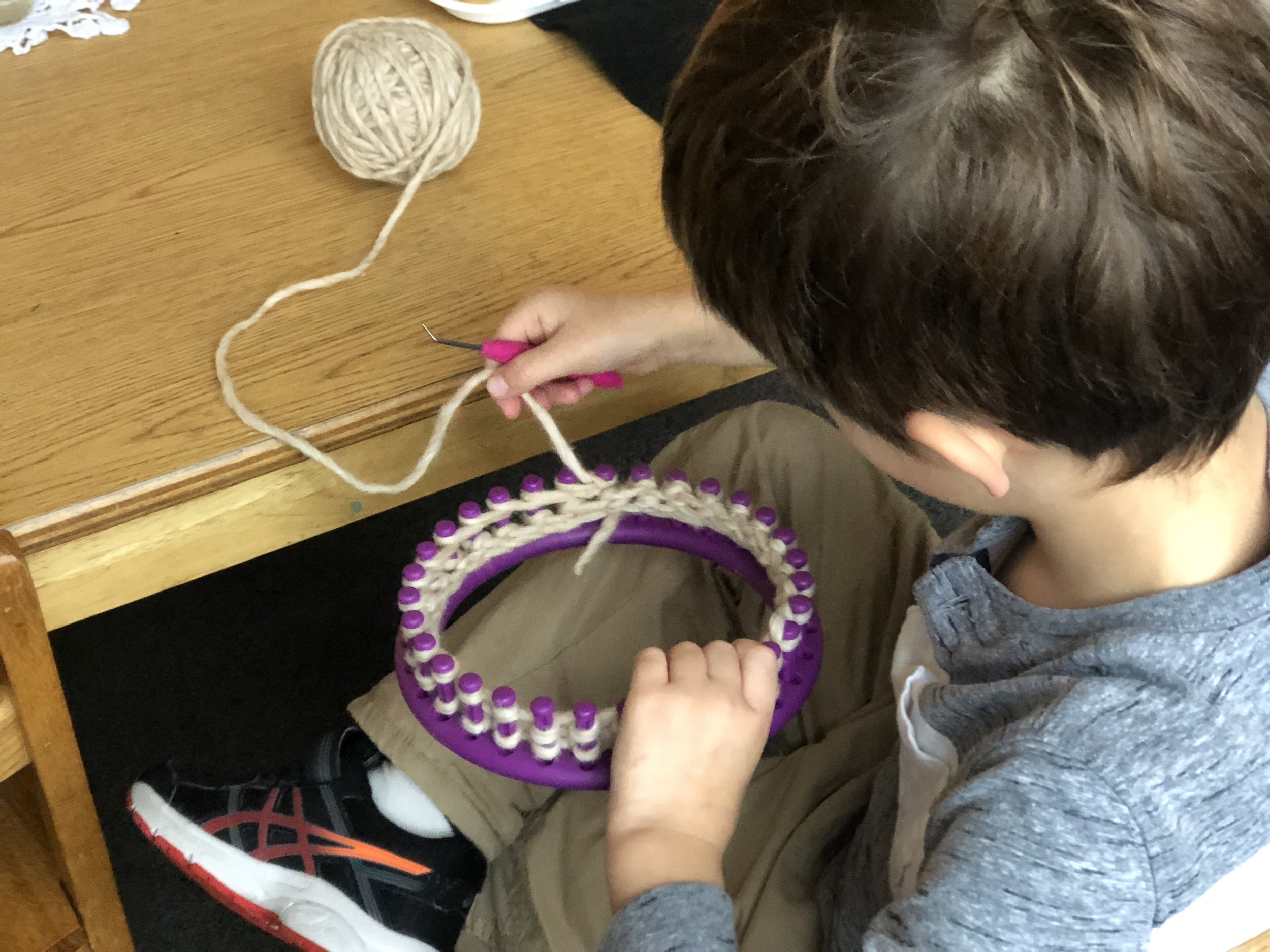  A student knitting on the loom to make a hat.  