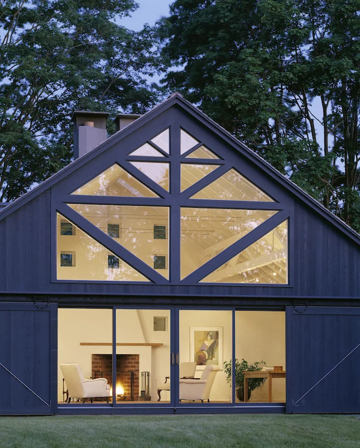 The small scale was maintained by making the additions a group of barn-like buildings in colors different from the original house. The master bedroom and a porte-cochere at the family entrance are simple, gable-roofed structures, painted barn red. The new “great room” structure is painted slate gray to blend into the shadow under the huge maple trees and the entrance and the sun room are painted spruce green, further differentiating its parts. The original house remains white, as the focal point of the composition.