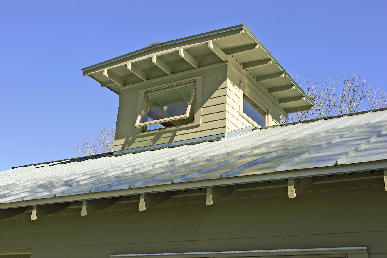Outside, a new broad roof overhang and galvanized metal roof protects new siding, windows and a welcoming four foot wide fir wood door. Two rooftop light monitors provide natural light and ventilation to the entry gallery and living space. Light falls into the existing and new space throughout the day. Inside, cedar posts and beams recall the branches of the pecan trees that protect the house. Interior walls are painted white, accented with natural finished fir wood lintels.