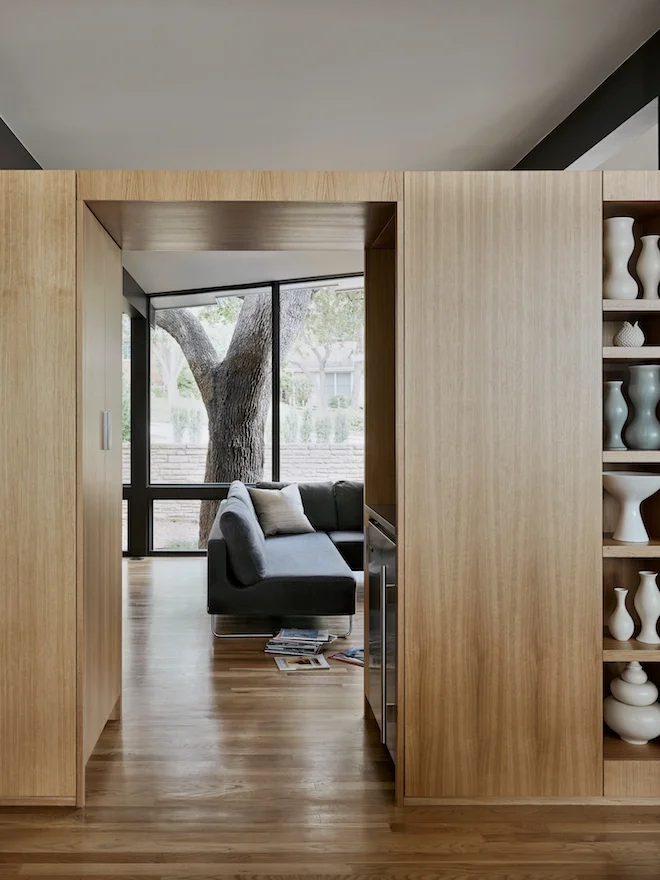 A new seven-foot high L-shaped white oak cabinet separating formal and informal living areas appears like another wall in the landscape. It contains the home’s artifacts and doglegs around a four-inch thick solid oak workbench-island built by an artist friend.