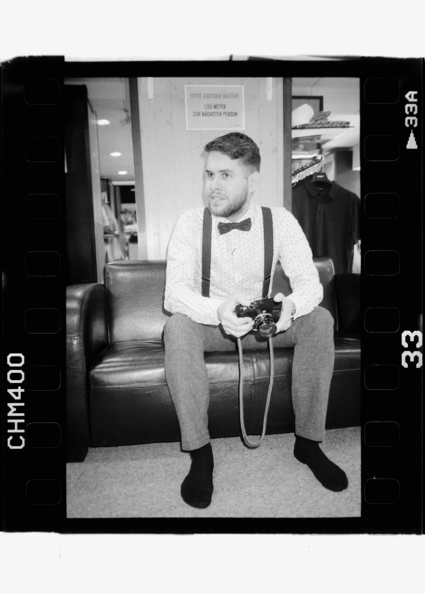 Der Fotograf Marvin Girbig in einer Schwarz Weiß Aufnahme mit Hemd und Fliege. In seiner Hand hält er seine Leica M Kamera.