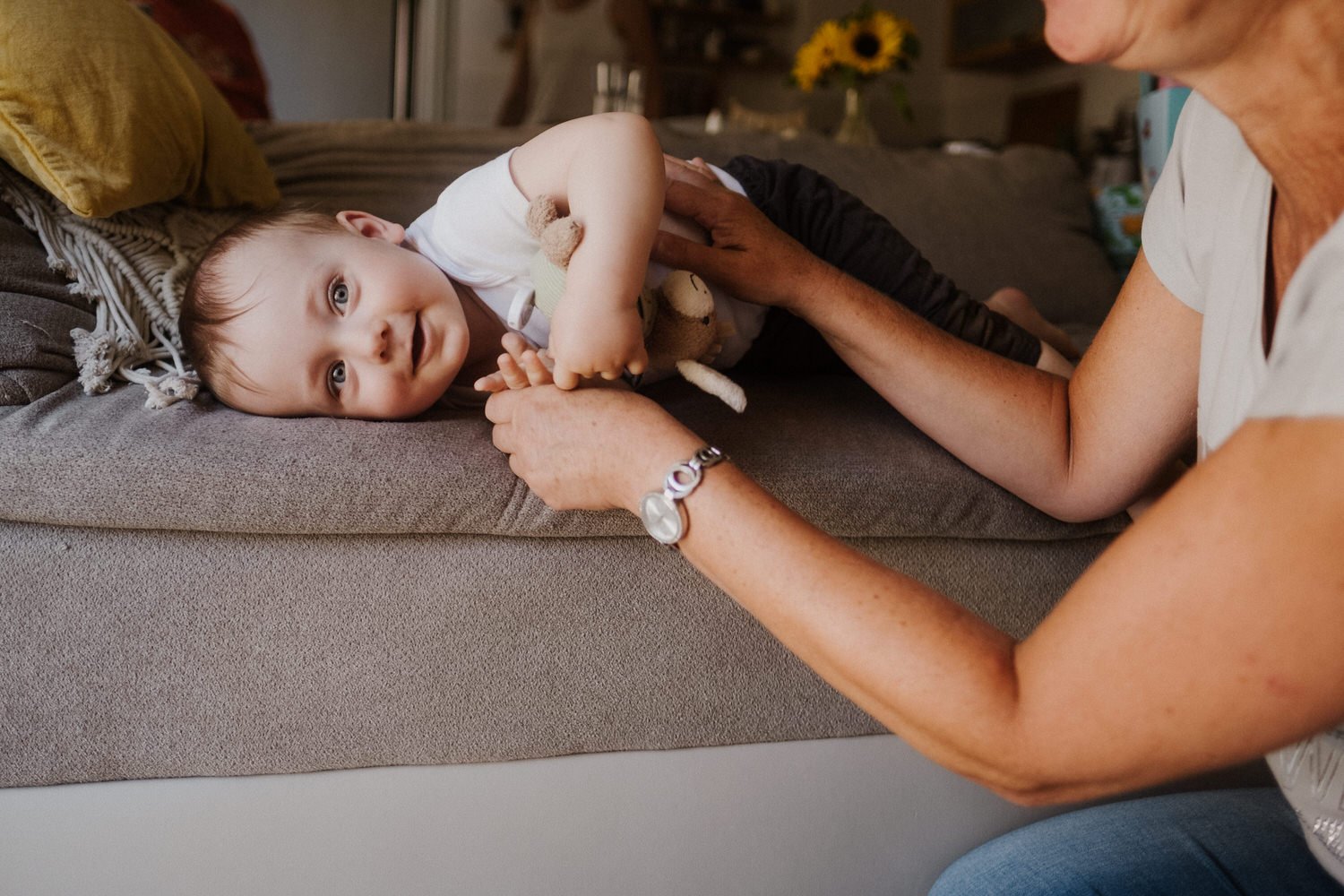Ein kleines Kind liegt auf einem Sofa und wird von einer Frau gestreichelt, während es lächelnd in die Kamera schaut.