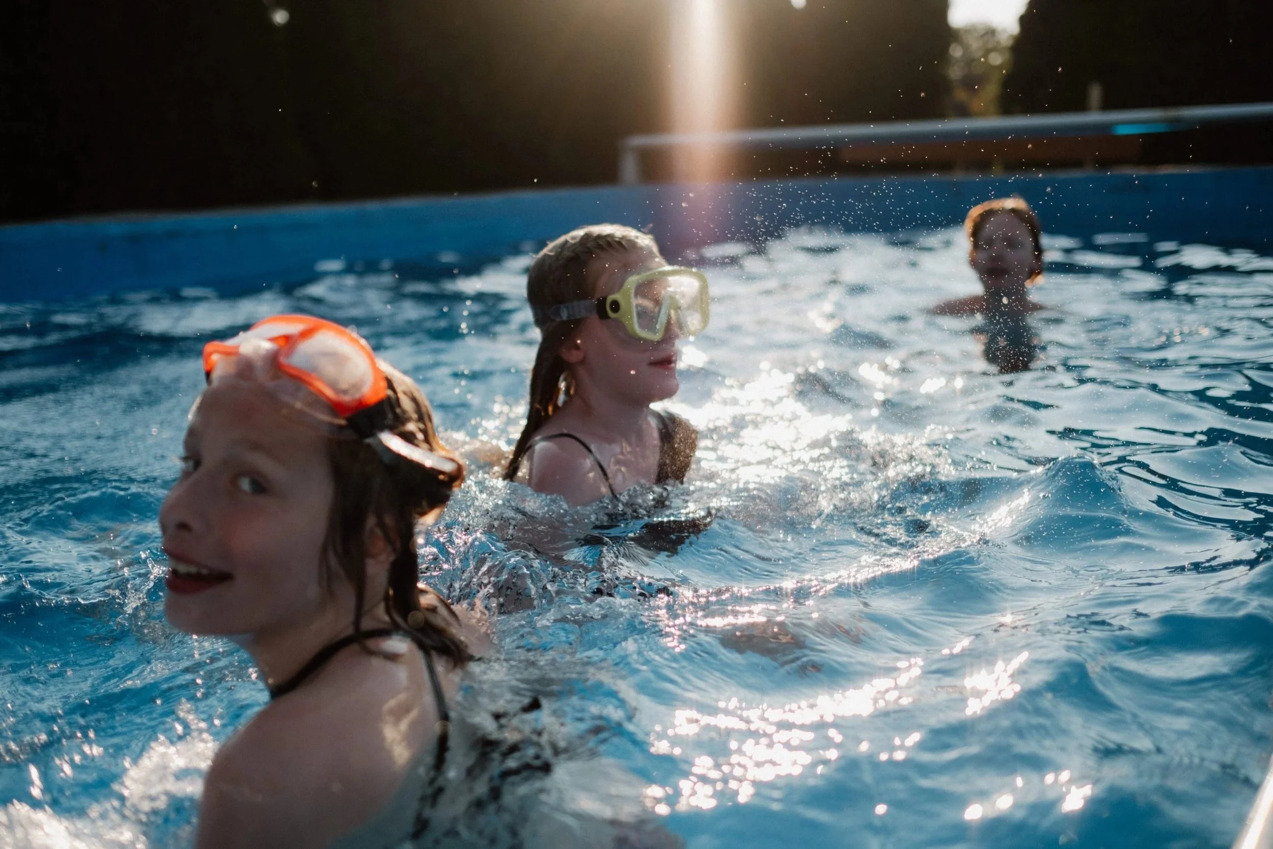 Ein schöner Moment mit viel Bewegung zeigt drei Kinder Spielens im Pool bei stimmungsvollen Sonnenlicht