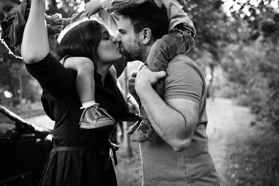 Ein herzlicher Moment zwischen Eltern die sich liebevoll küssen während sie Ihre Kinder auf dem Schulter tragen.