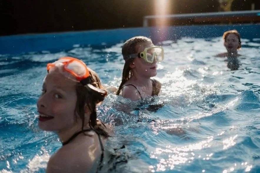 Während einer Familienreportage sind drei Kinder zu sehen, die in einem Außenpool schwimmen, bei Sonnenuntergang