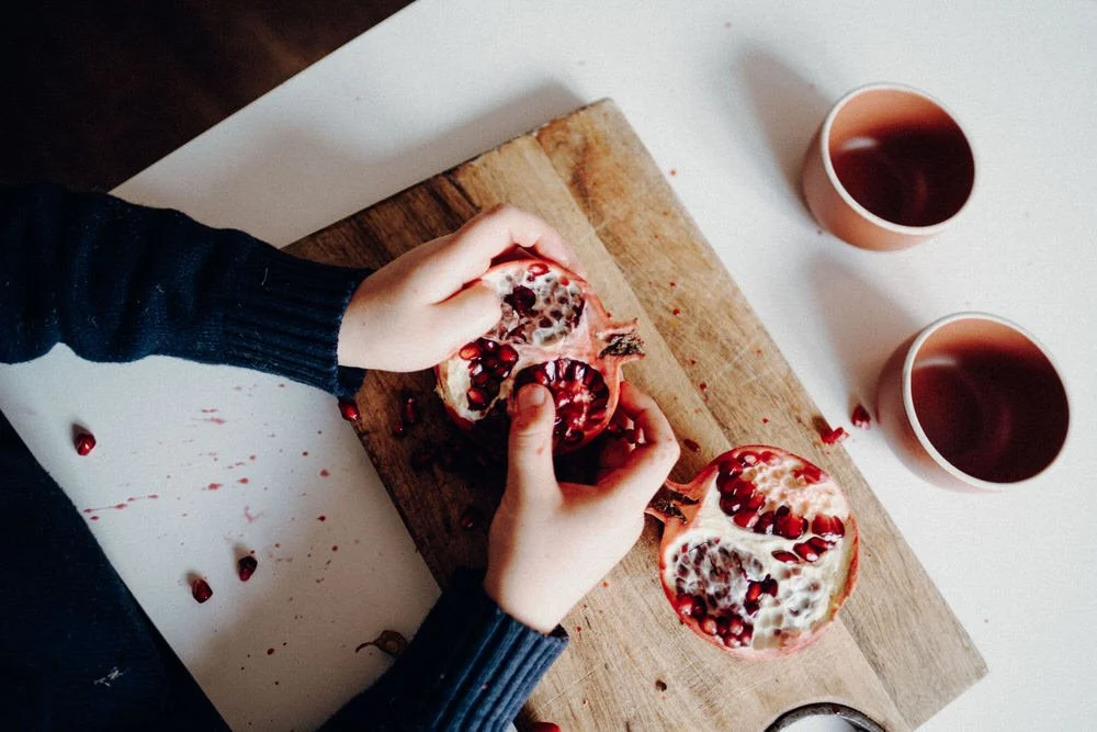 Kind entkorkt Granatapfel auf einem Schneidebrett, die Oberfläche hat Flecken und Granatapfelkerne.