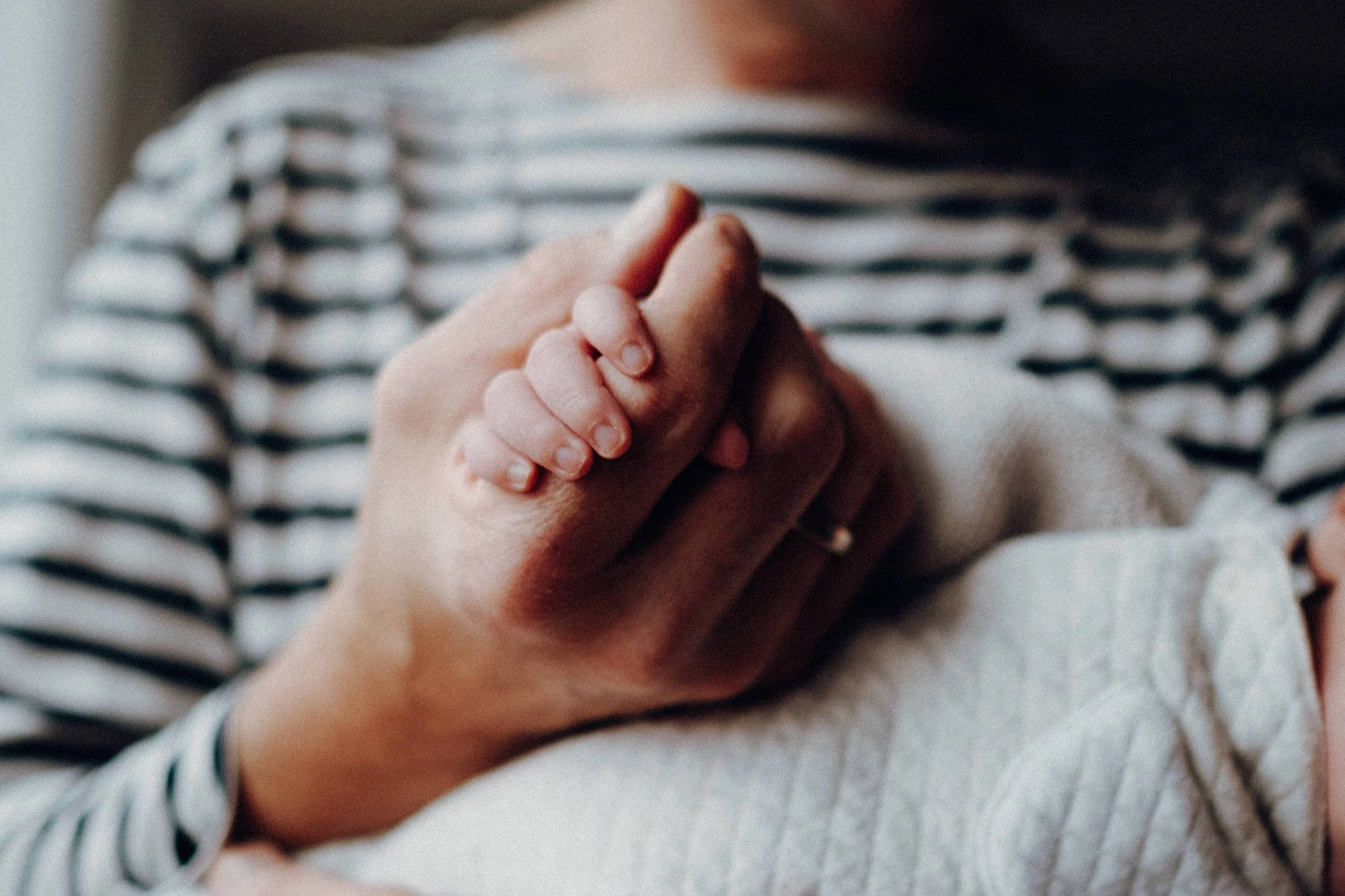 Detailaufnahme von der großen Hand eines erwachsenen Mannes und der kleinen Hand eines Babys, das bei einem Neugeborenen Fotoshooting entstand. Der Größenunterschied verdeutlicht das junge zarte Alter des Babys und dem Beschützerinstinkt des Vaters.