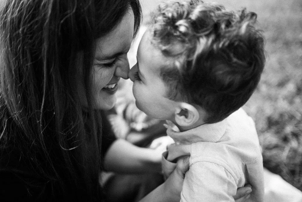 In der Schwarz-Weiß Nahaufnahme geben sich Mutter und Sohn freudig einen Nasenkuss. Diese Aufnahme zeigt die Innigkeit und Nähe der beiden zueinander.
