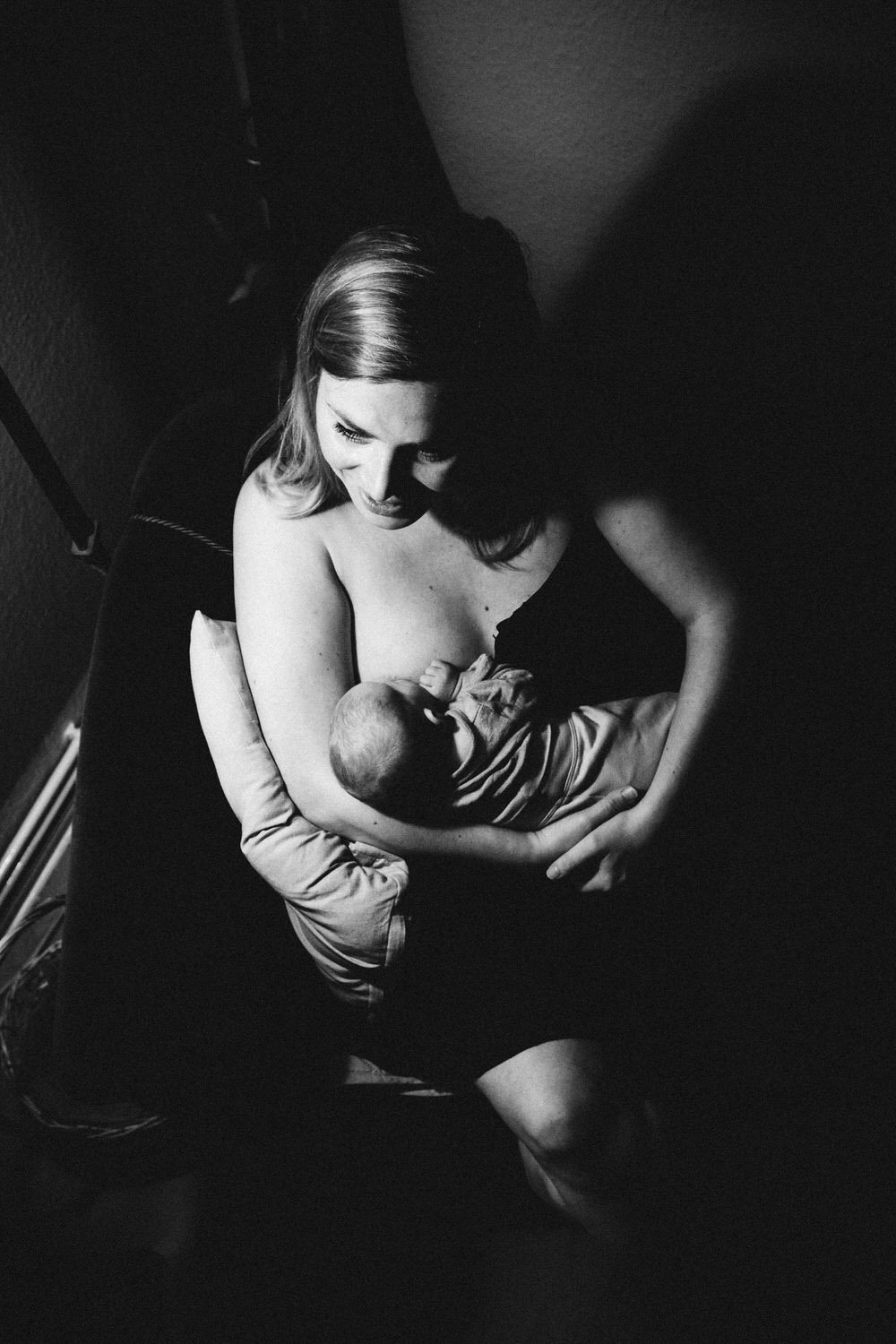 Schwarz-weiß-Foto einer Mutter, die ein Baby stillt, in einer ruhigen, intimen Szene.