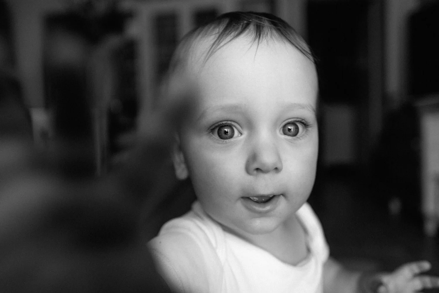 Nahaufnahme eines lachenden Babys mit leuchtenden großen Augen, das den Betrachter anschaut, in Schwarz-Weiß. Er greift nach der Kamera.