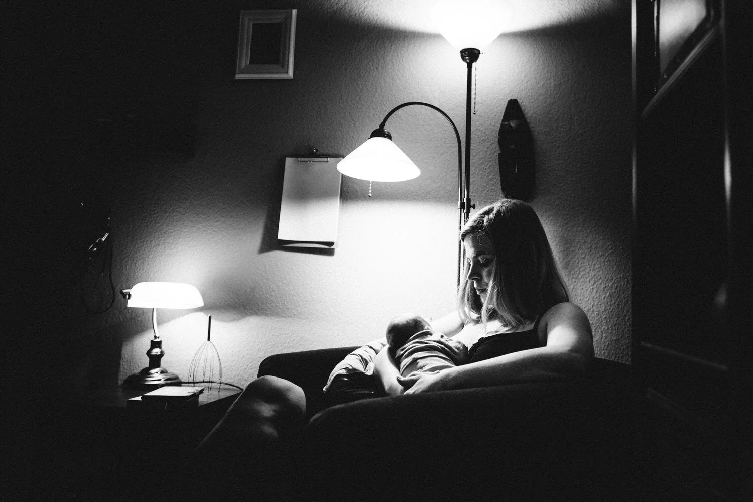 Frau stillt ein Baby auf einer Couch bei schwachem Licht in einem dunklen Raum.