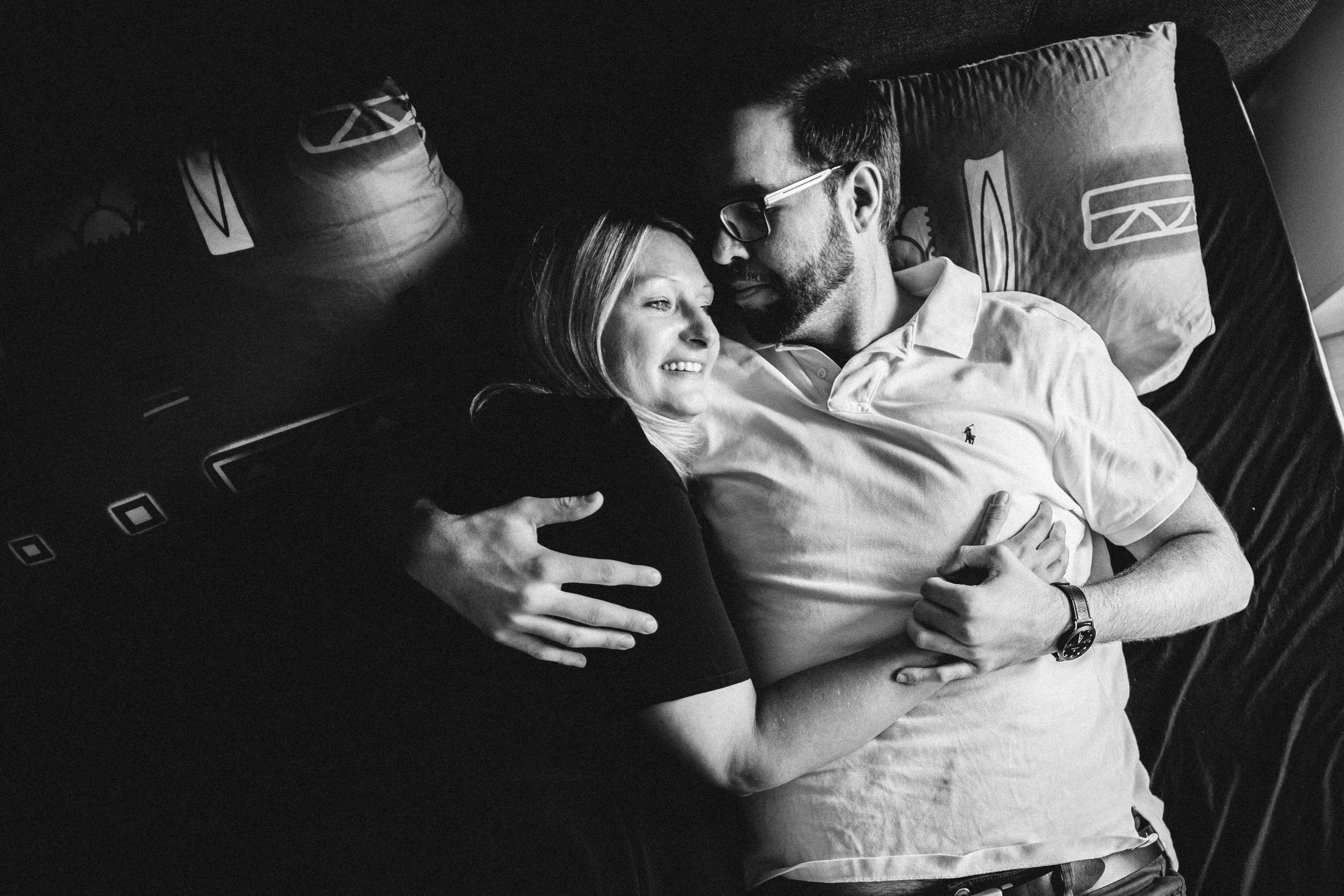 Im Bett liegend sieht man bei der monochromen Aufnahme ein kuschelndes Pärchen. Das natürliche Licht fällt Stimmungsvoll von der Seite rein.