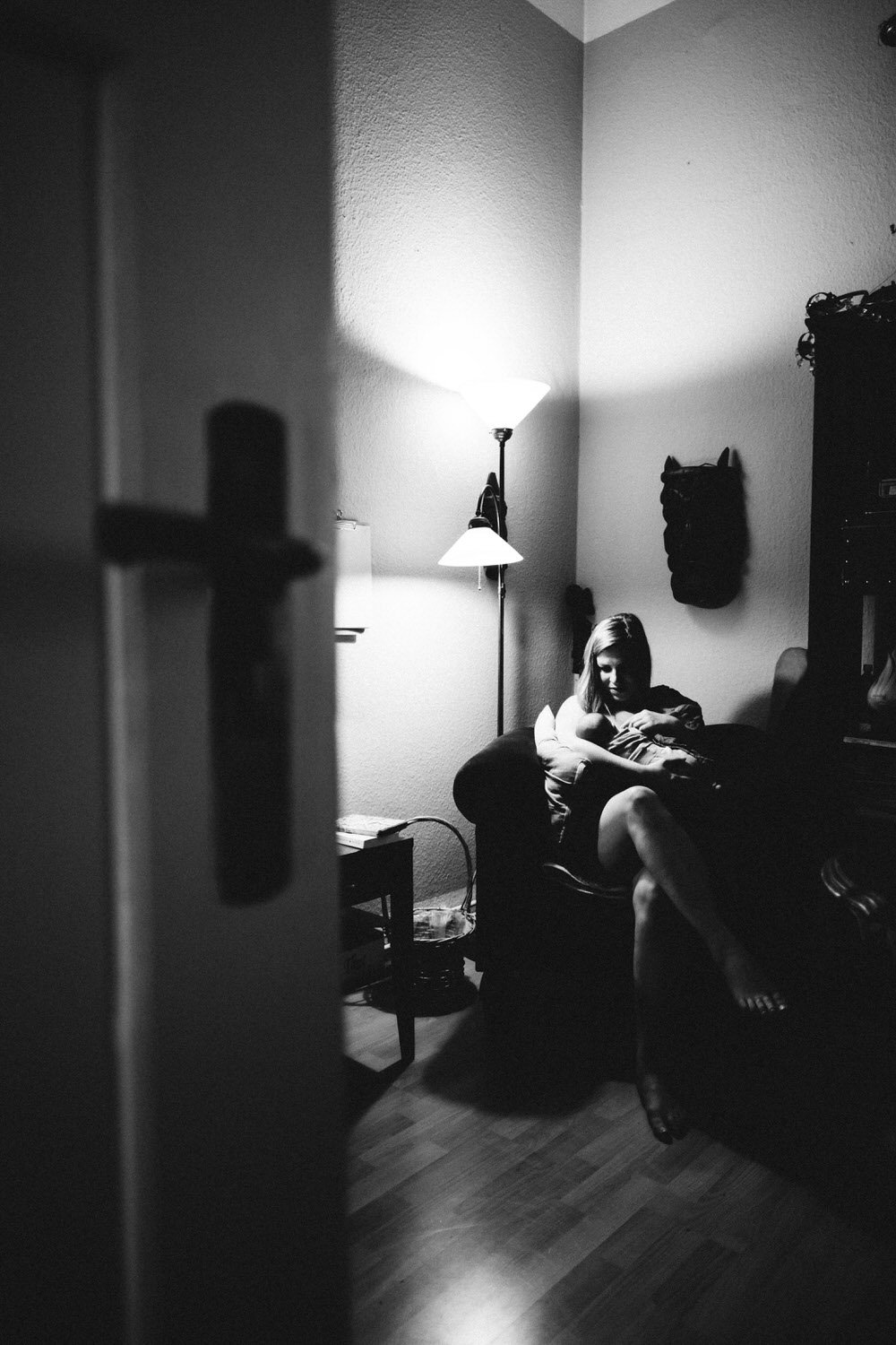 Schwarz-weiß-Foto einer Mutter, die in einem Sessel sitzt und ihr Baby bei gedämmten Licht stillt.