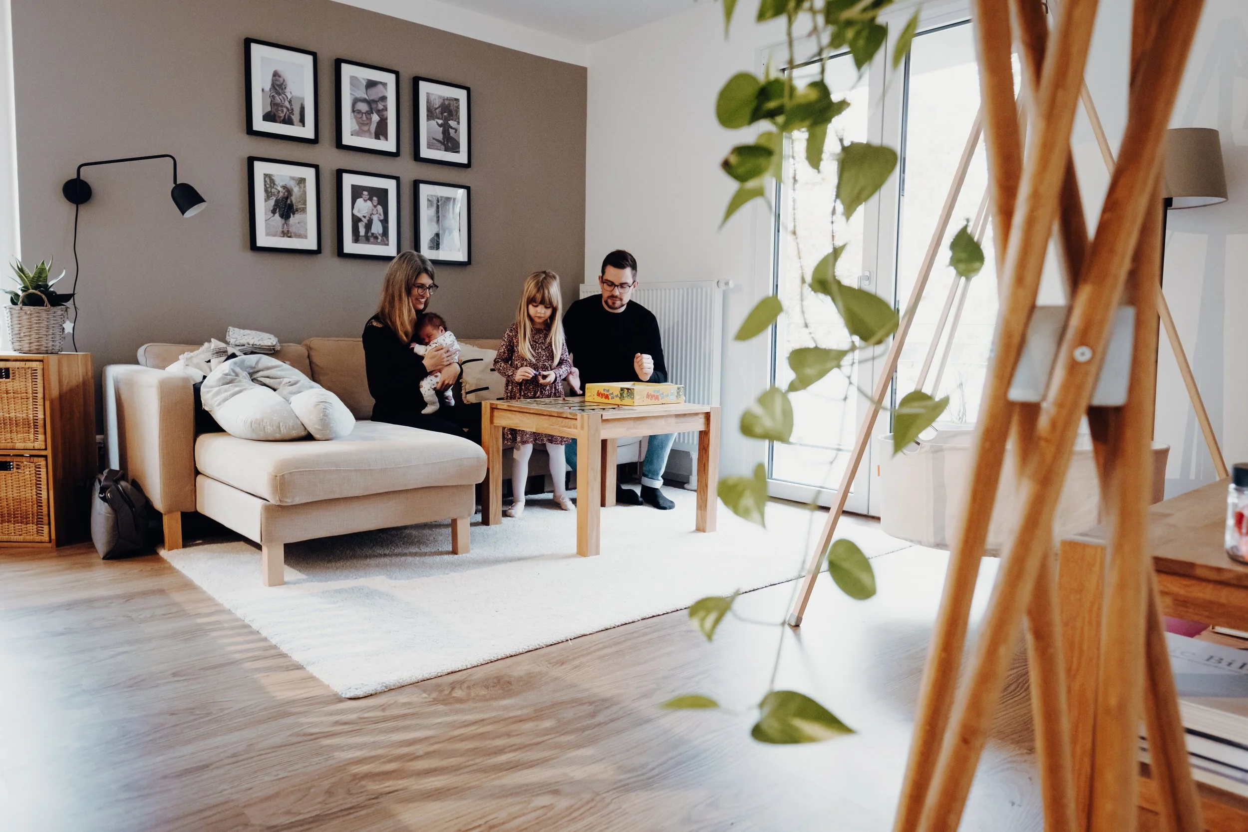 Eine Familie sitzt während eines Homestory Fotoshoot im hellen Wohnzimmer auf der Couch und spielen vergnügt ein Brettspiel.