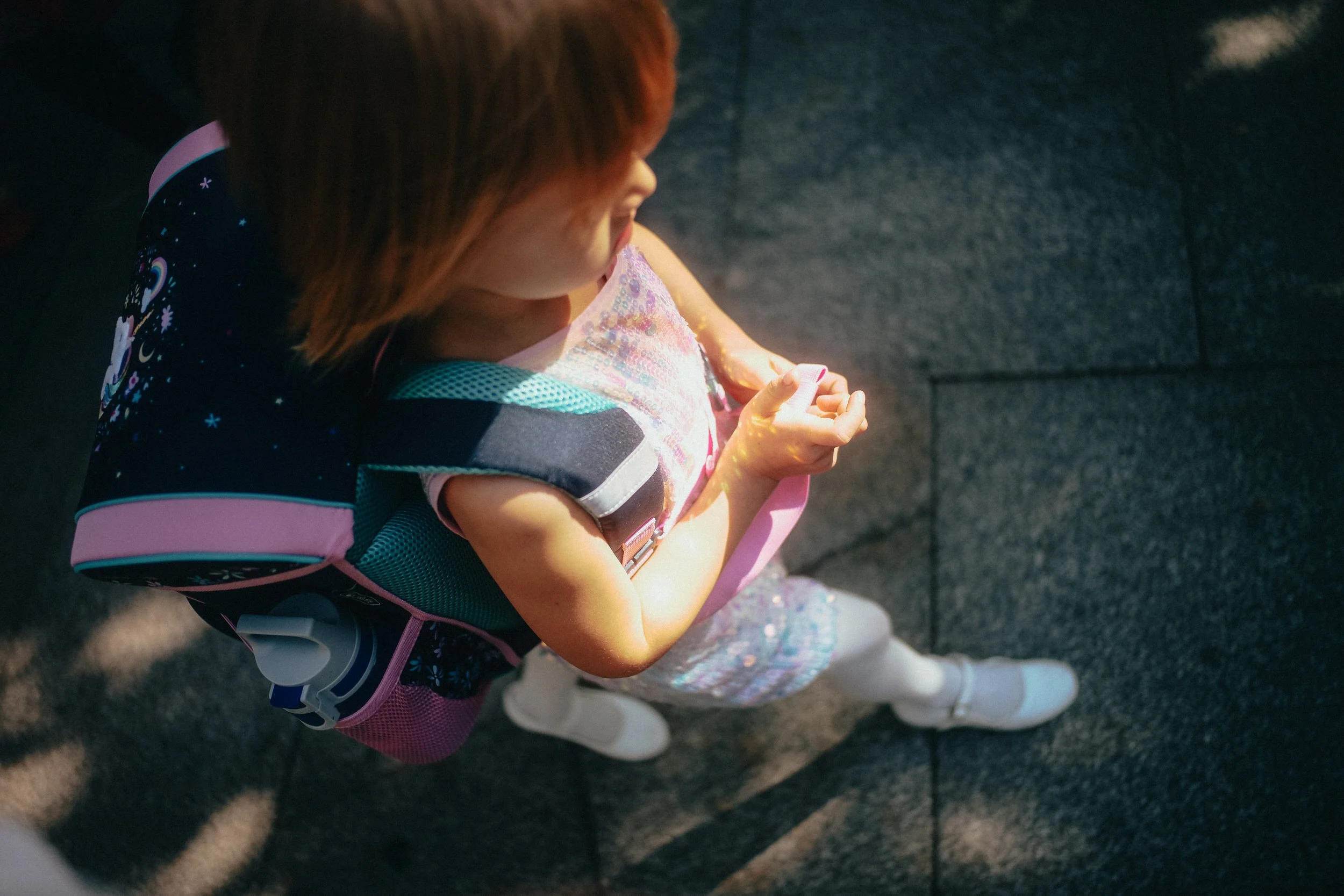 Ein Kind mit Rucksack geht über eine Straße. Sie wird vom Licht angestrahlt und ihr Glitzerkleid leuchtet