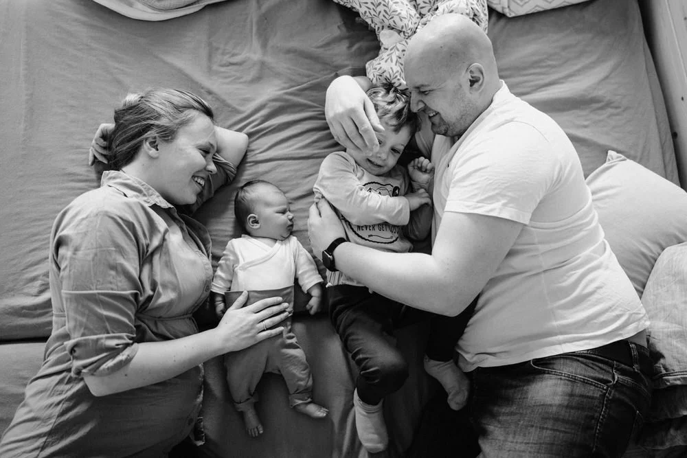 In dieser zu Hause Reportage sieht man eine Familie mit zwei kleinen Kindern liegt lachend im Bett, Vater umarmt den älteren Sohn, Mutter hält das Baby.