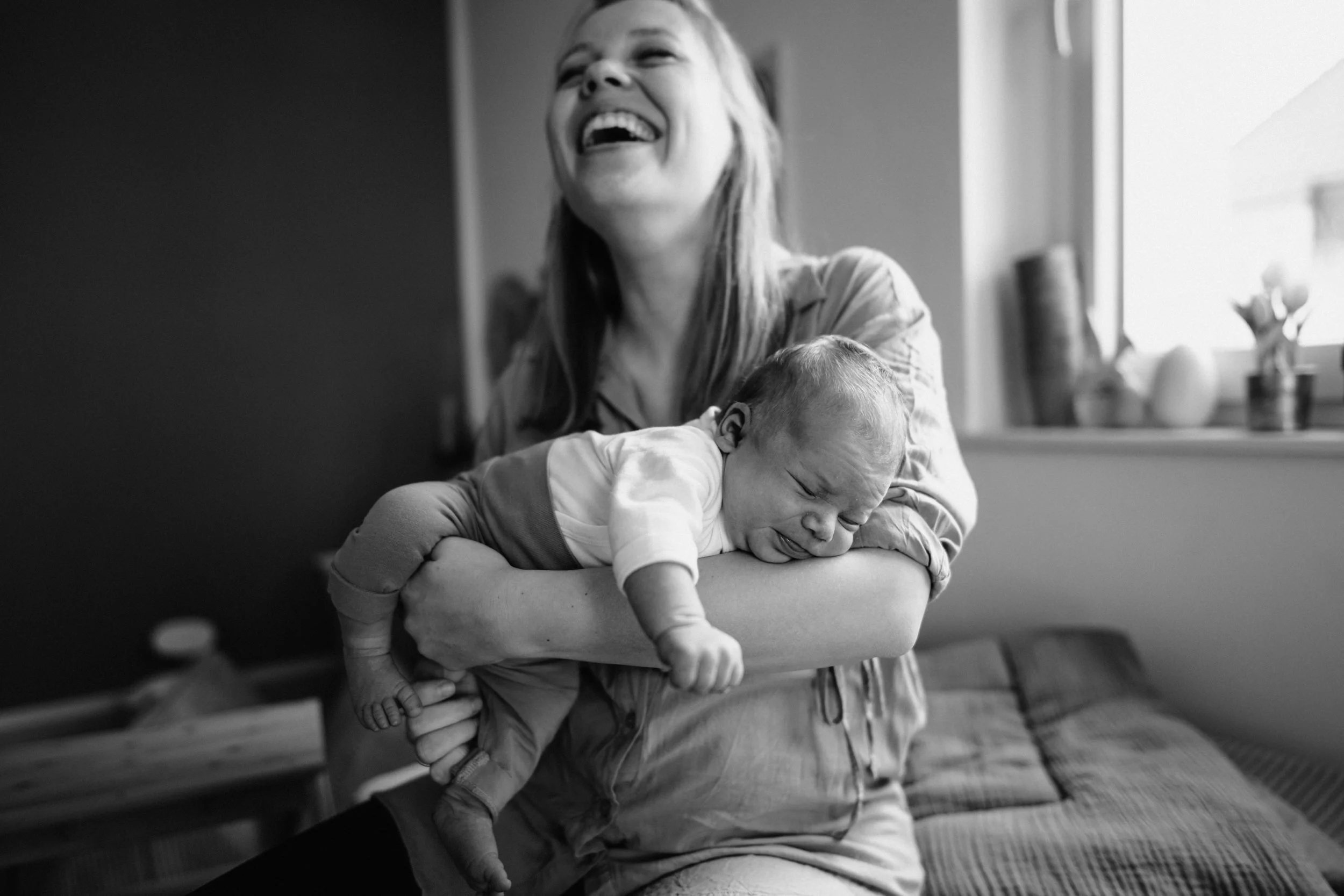 Eine junge Mutter hält ihr Baby auf den Arm und lacht ganz herzlich - eine authentische Momentaufnahme.