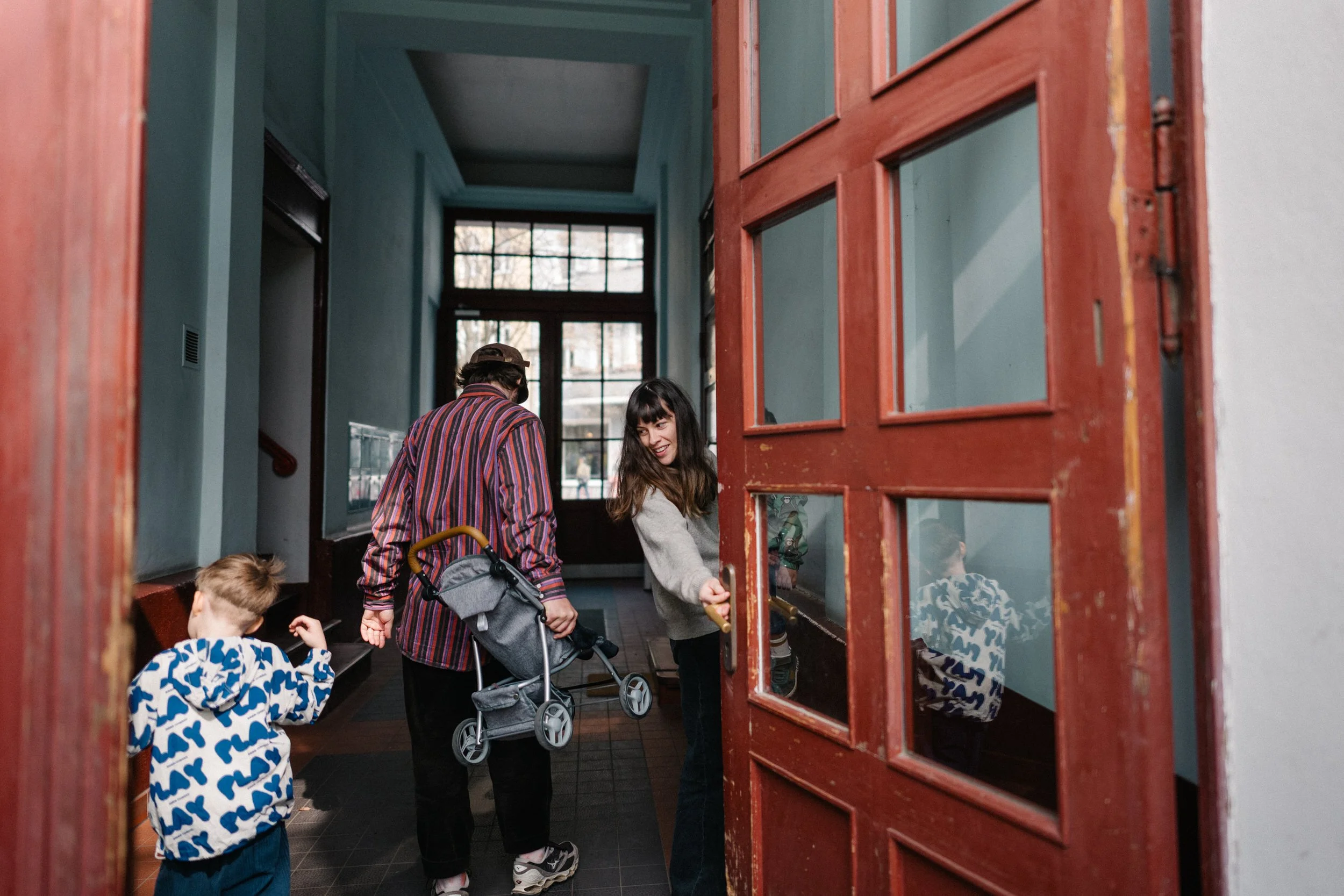 Eine Familie betritt den Hausflur eines Berliner Altbaus in Friedrichshain durch eine rote Holztür