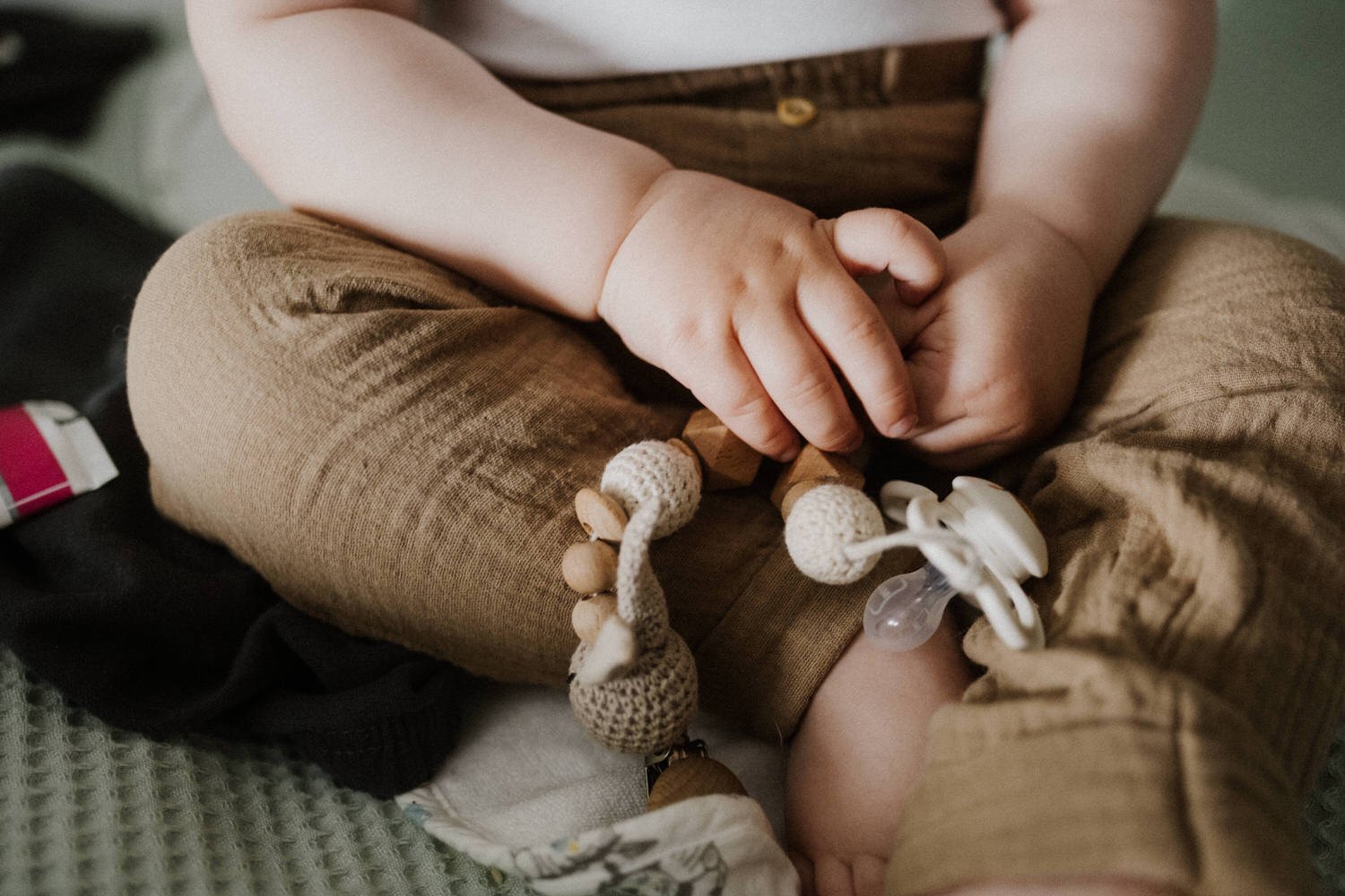 Nahaufnahme der Hände eines Kindes, das im Sitzen ein Stofftier und Nuckel hält.