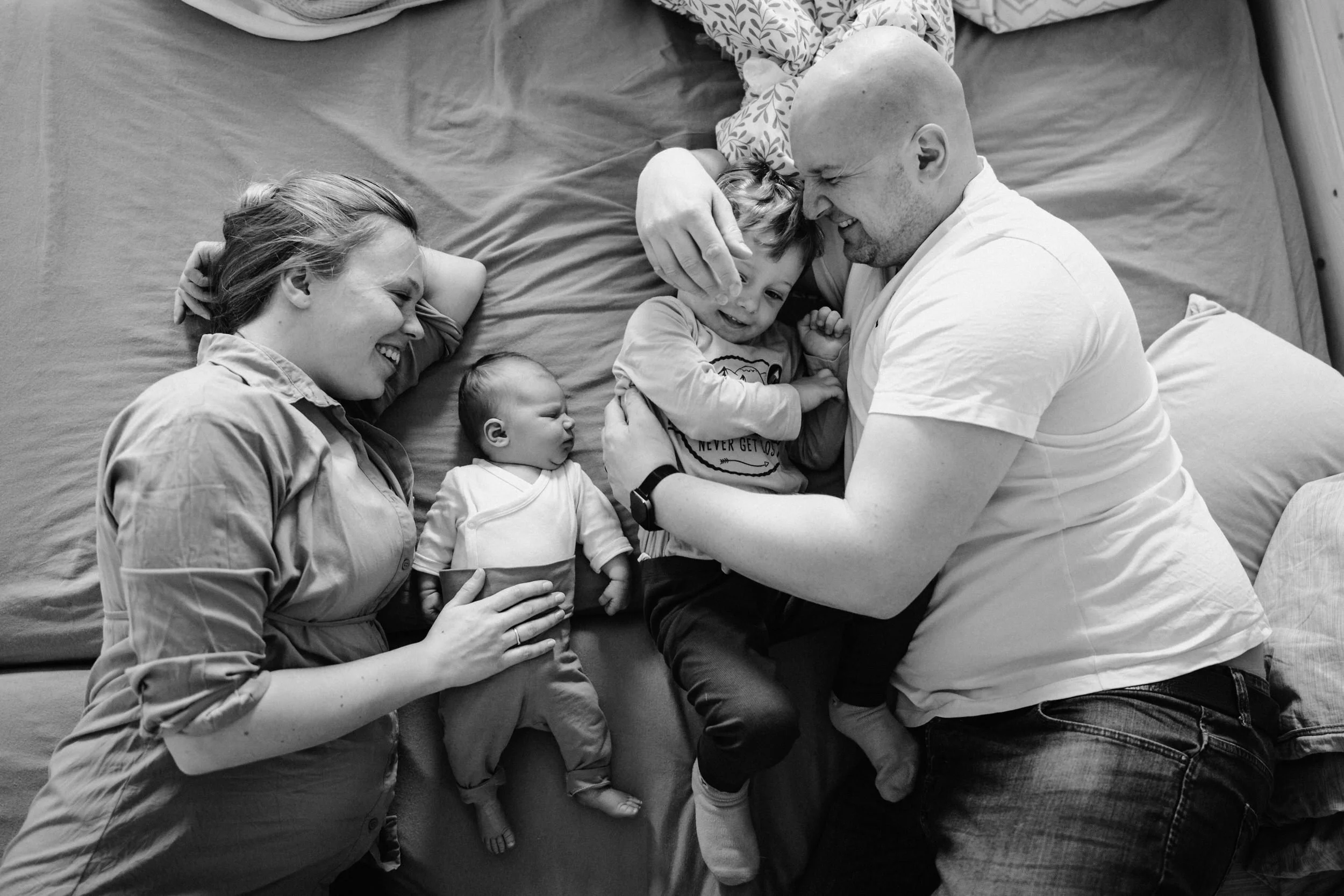 Während einer Homestorie fotografierte Familie im Bett liegend, die miteinander lachen und kuscheln. Ein toller und fröhlicher Augenblick.