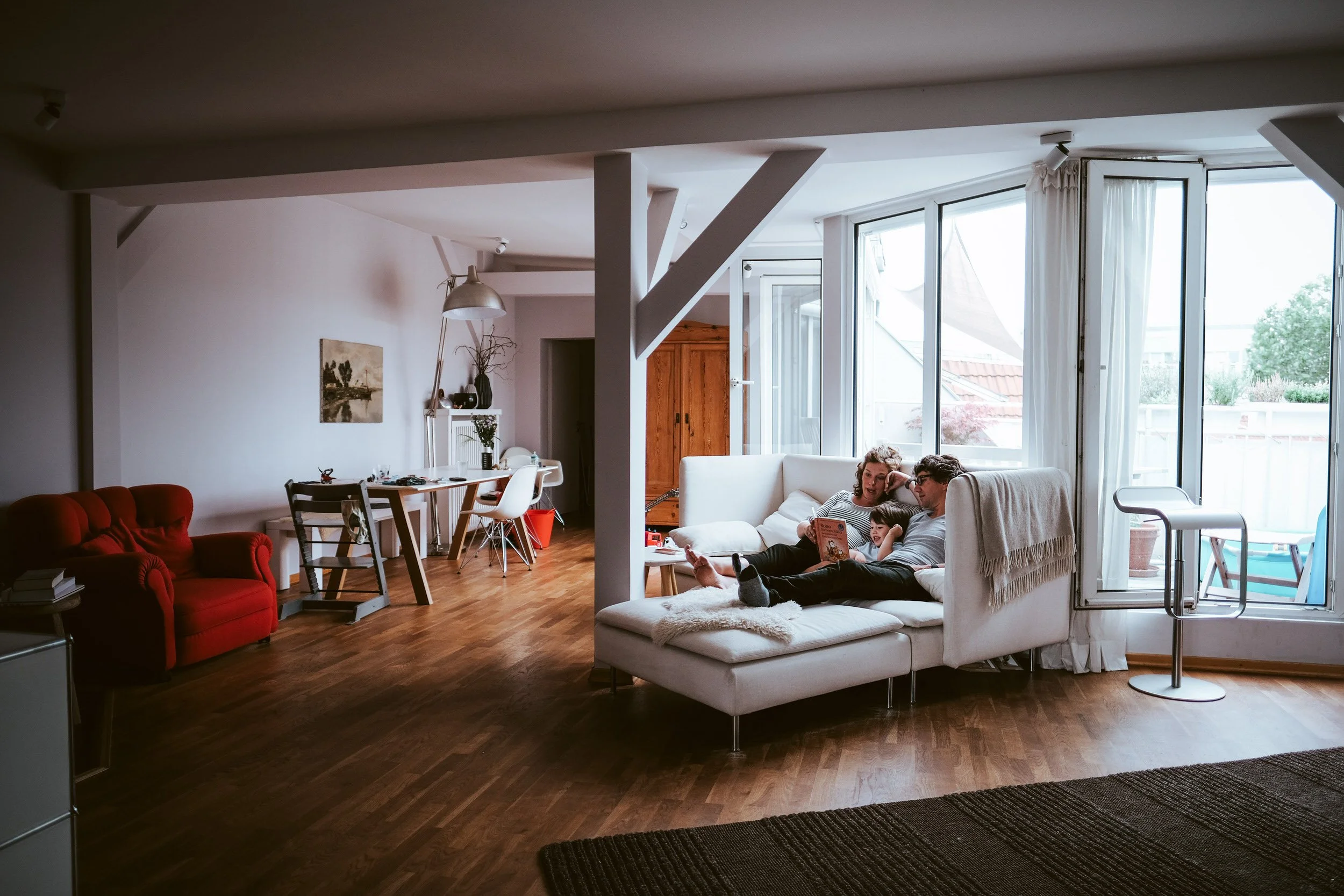 In einer große und hellen Wohnung in Berlin sieht man während einer Homestorie eine Familie auf dem Sofa liegend. Sie lesen in der Alltagssituation ihrem Kind ein Buch vor.