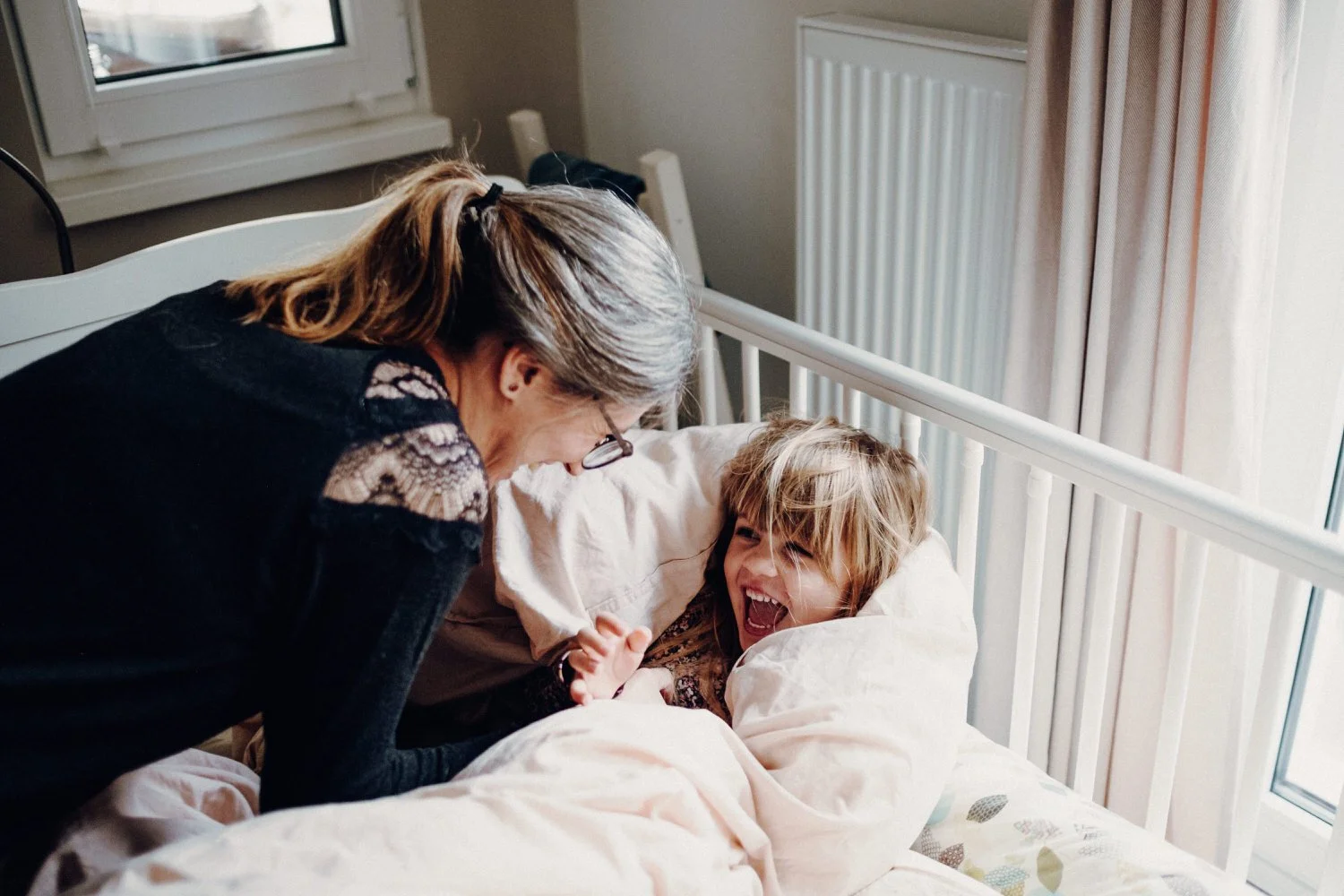 Mutter und Tochter lachen und spielen harmonisch und innig zusammen im Bett.