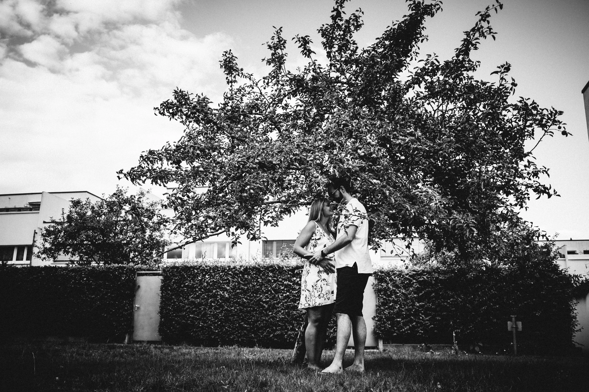 Paarumarmung unter einem Baum in einem Garten, in schwarz-weiß aufgenommen.