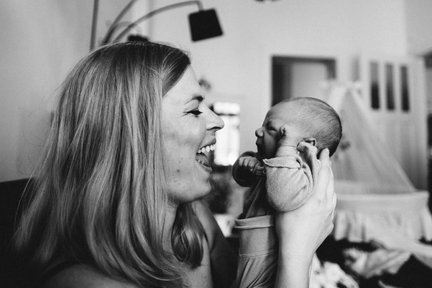 Authentischer Moment: Lächelnde Frau hält ein Baby im Arm, beide schauen sich an, Schwarz-Weiß-Foto.