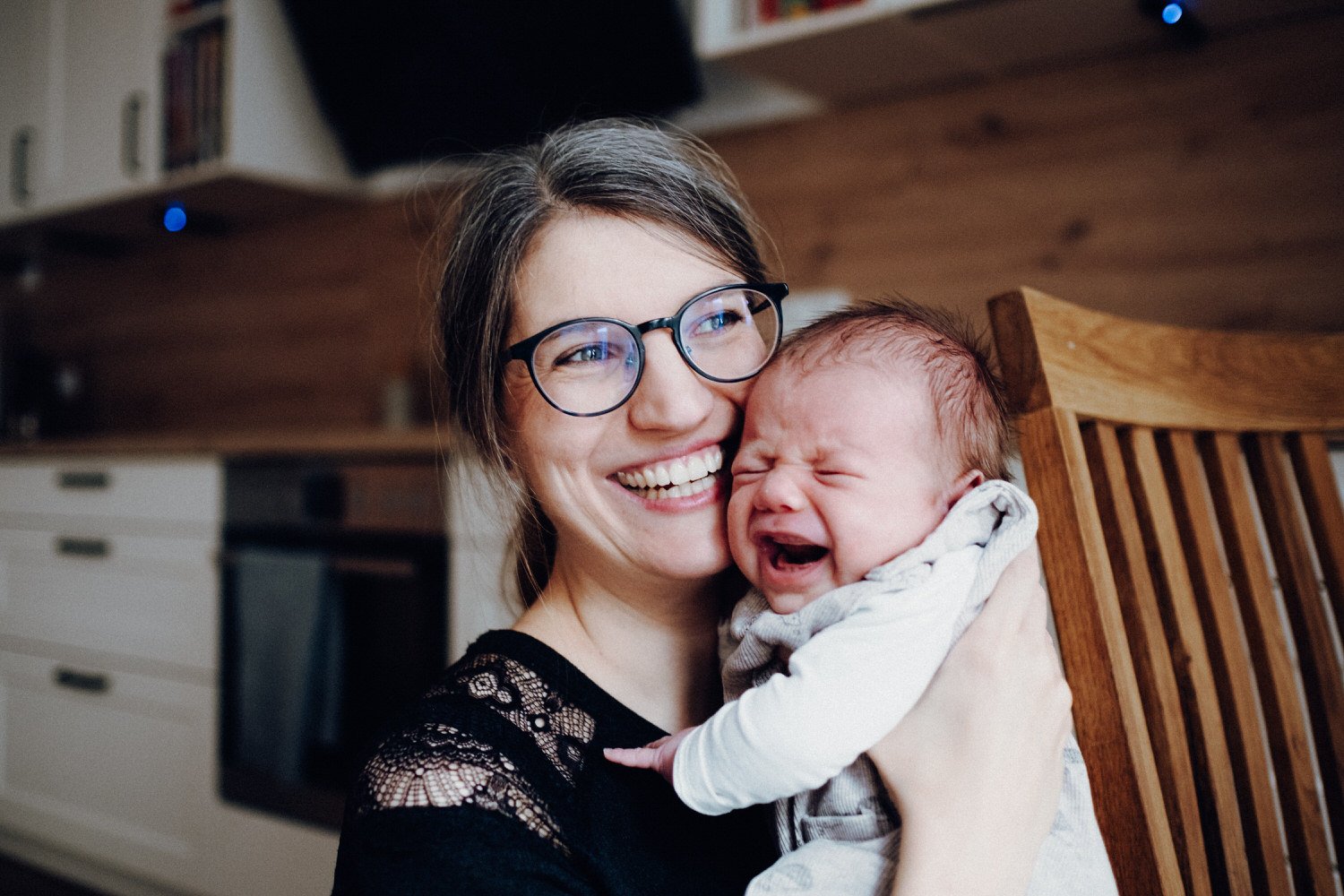 Eine authentische Alltagsszene: Eine Frau mit Brille hält ein weinendes Baby in den Armen.