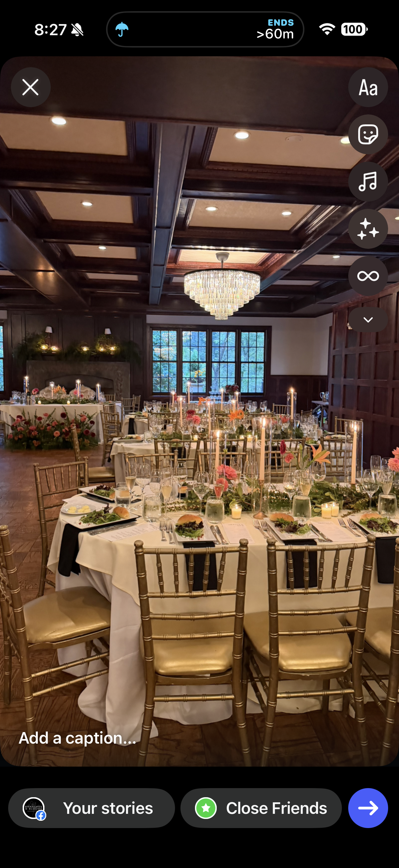 Elegant banquet hall decorated for a formal event with round tables covered in white tablecloths, floral centerpieces, candles, and place settings including plates, silverware, and glasses. Gold chairs surround the tables, and a chandelier hangs from