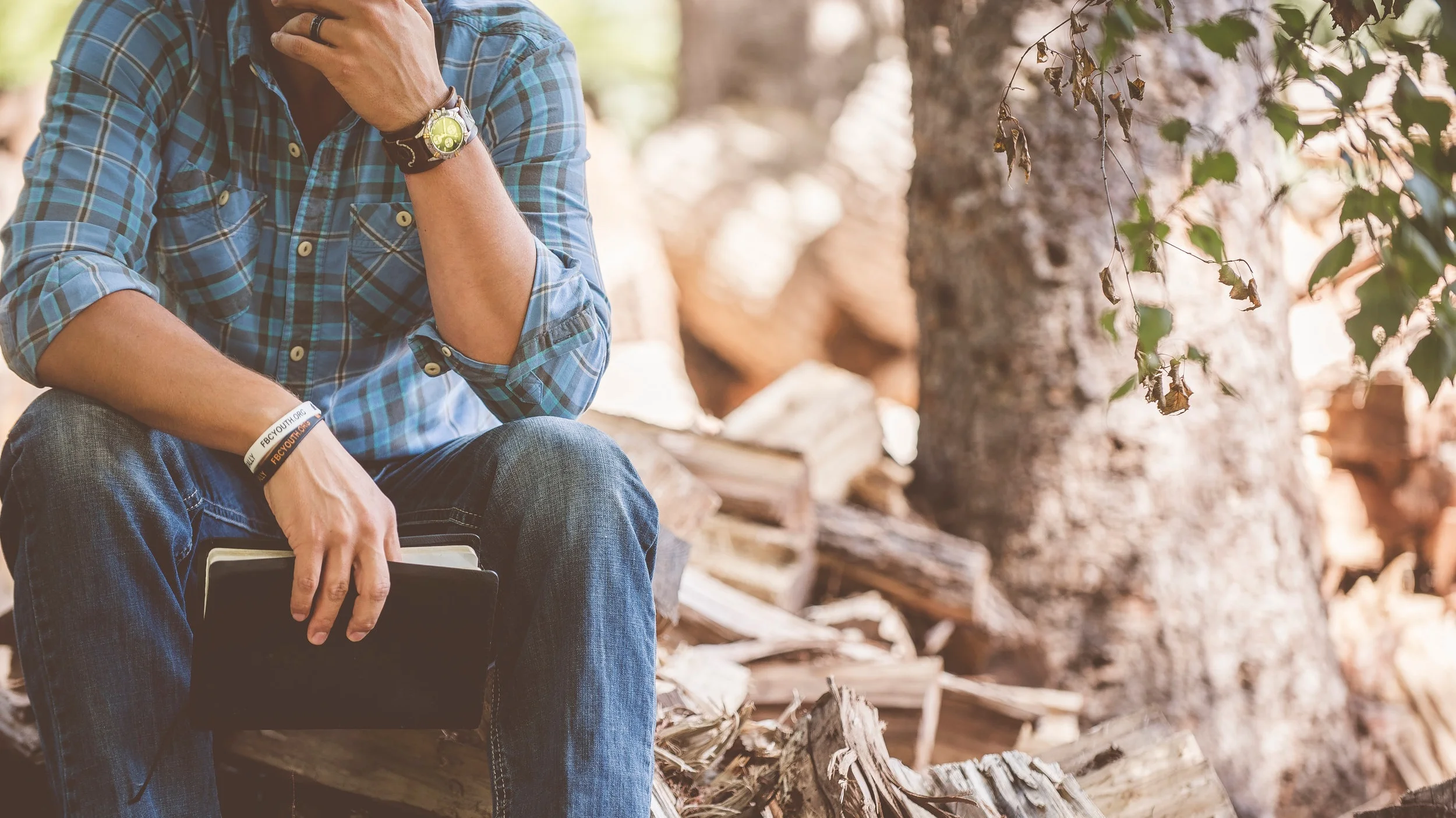 Man sitting on a stump, holding a Bible, with his head in his hand.