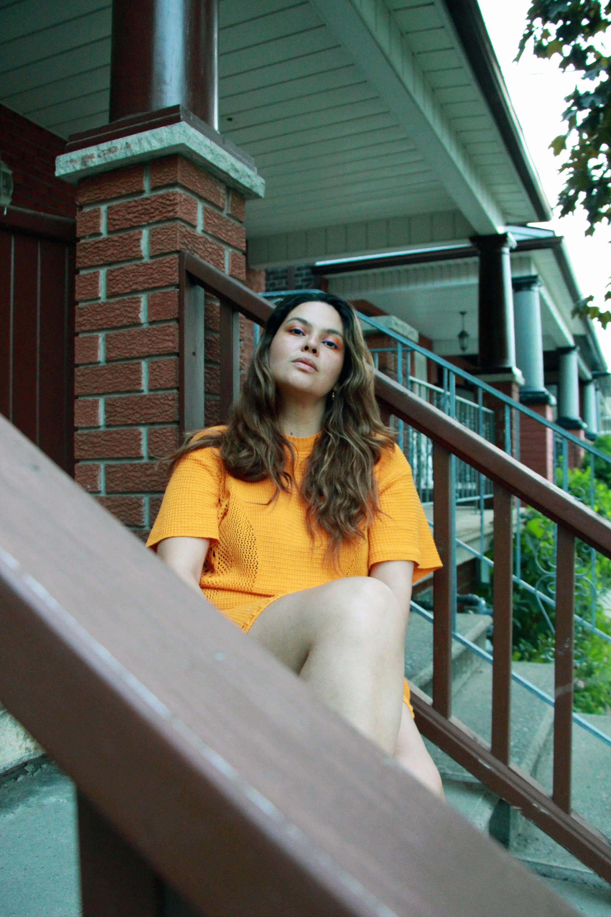 A woman with long brown hair in a marigold yellow dress sits on steps of a house. 