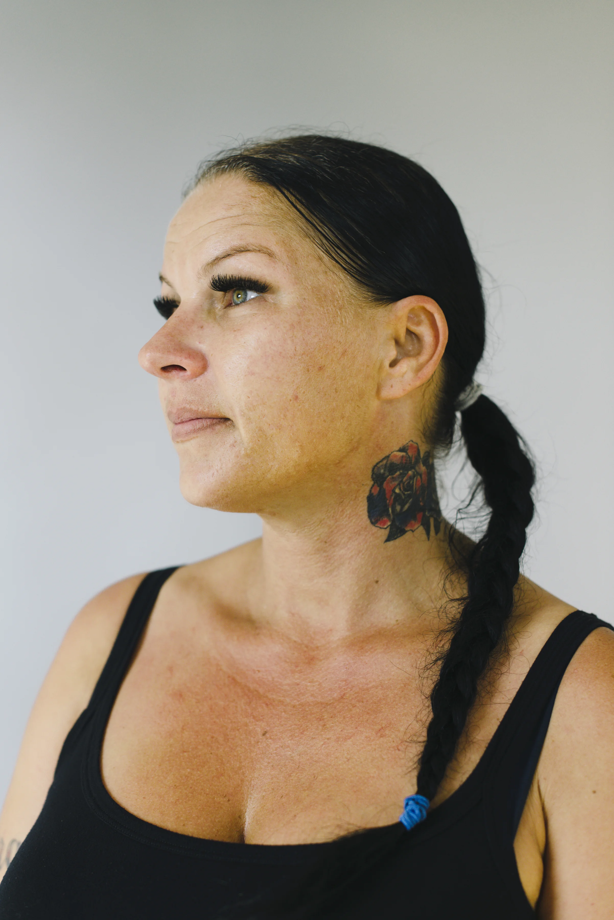Side profile studio portrait of a woman with a braided hair and a neck tattoo, looking toward a window with a relaxed expression