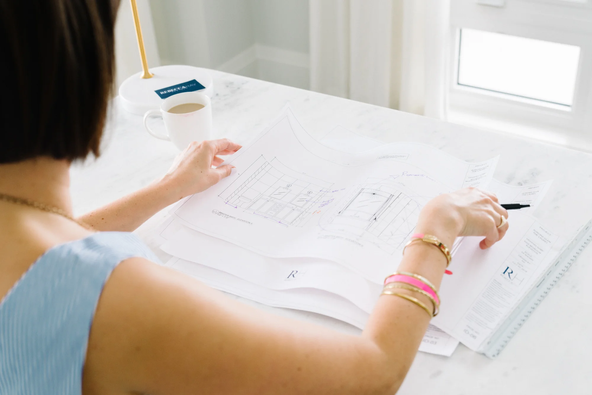 Over the shoulder lifestyle photo of Rebecca Hay reviewing interior design schematics at her workspace