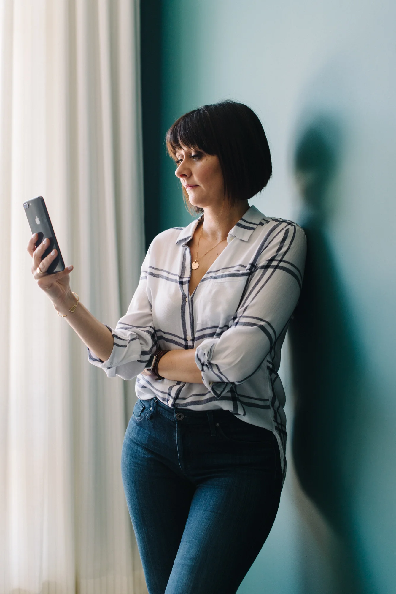 Lifestyle portrait of Rebecca Hay leaning against a wall working on her phone